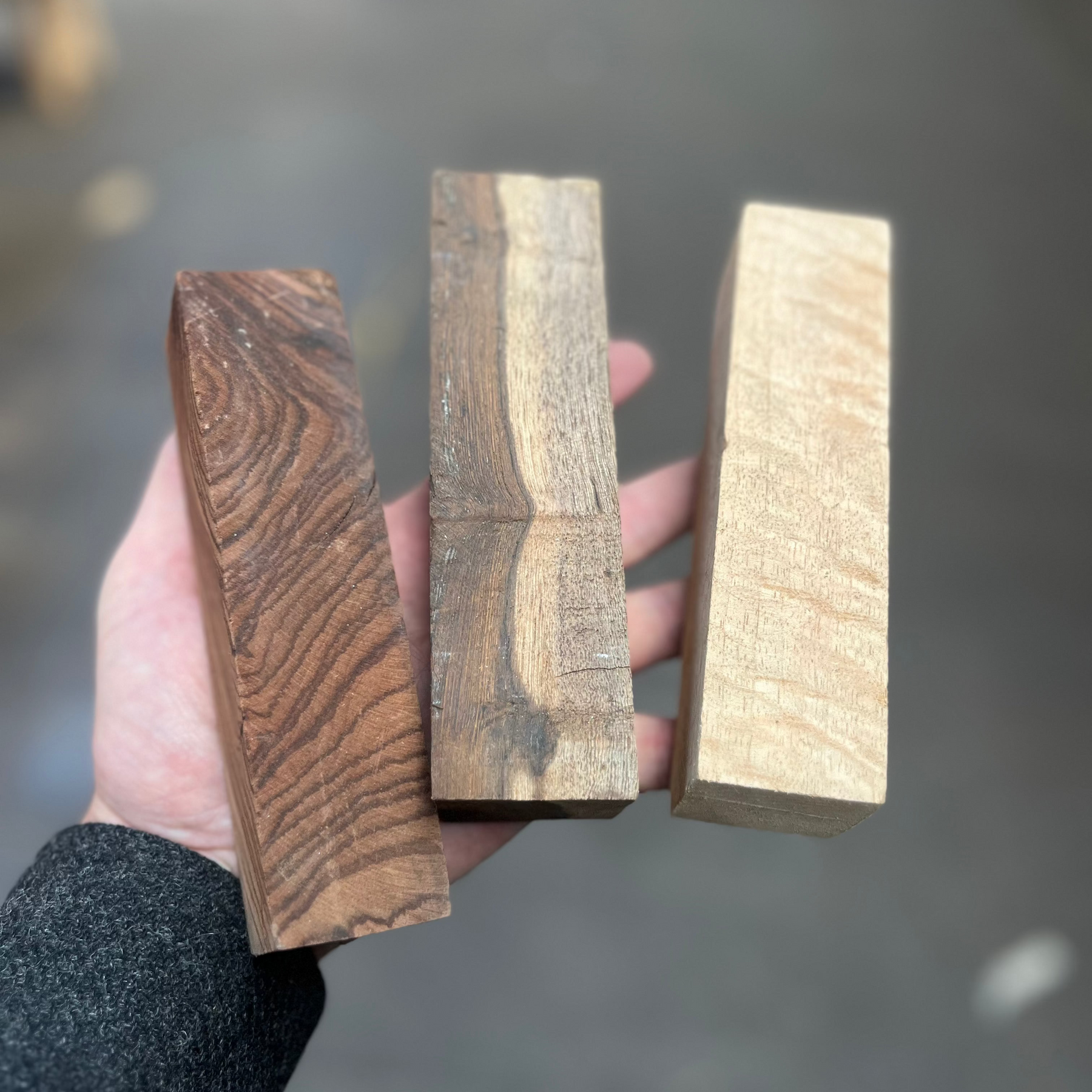 Three exotic hardwood turning blocks held in hand, showing contrasting dark, streaked and pale grain