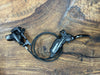 A black SRAM hydraulic disc brake lever and caliper assembly with a coiled black cable, displayed on a rustic wooden surface.