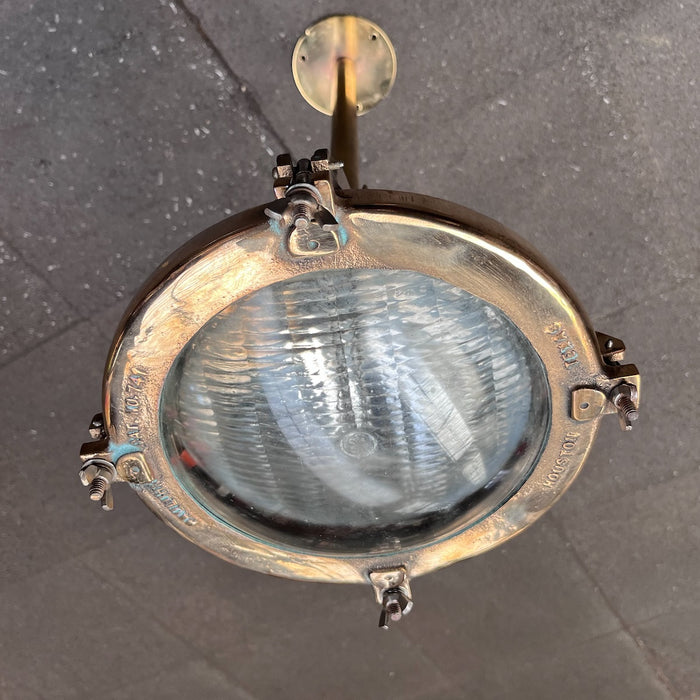 Salvaged Pauluhn 741 brass marine spotlight hanging from a brass drop rod and ceiling plate, ribbed glass lens facing down