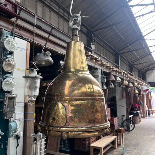 Salvaged brass ship's searchlight converted into a hanging pendant light, with the bell-shaped brass housing and caged glass lens visible from below.