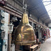 Salvaged brass ship's searchlight converted into a hanging pendant light, with the bell-shaped brass housing and caged glass lens visible from below.