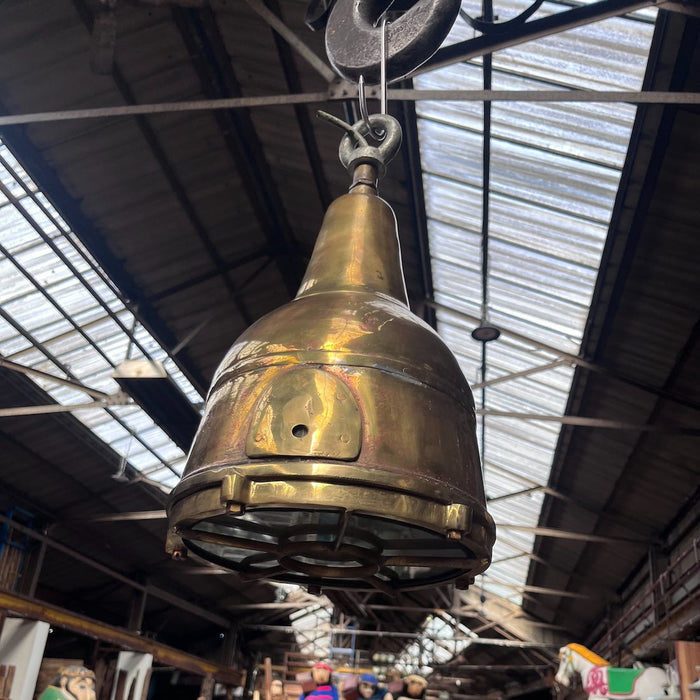 Side view of the salvaged brass ship's searchlight pendant light, showing the original hinged access plate and mounting holes from its days as a working searchlight.