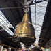 Side view of the salvaged brass ship's searchlight pendant light, showing the original hinged access plate and mounting holes from its days as a working searchlight.
