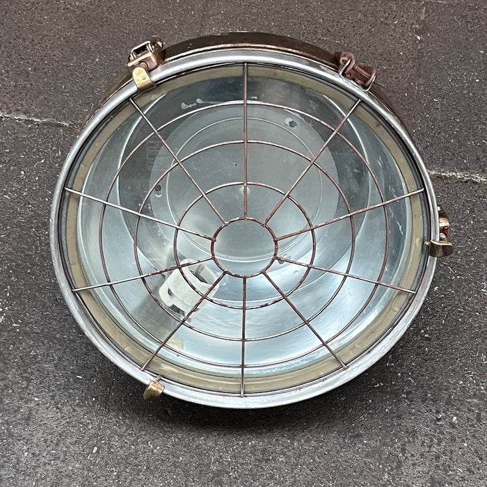 Front view of vintage VEB cargo ceiling light with circular wire guard, glass cover and brass toggle clamps