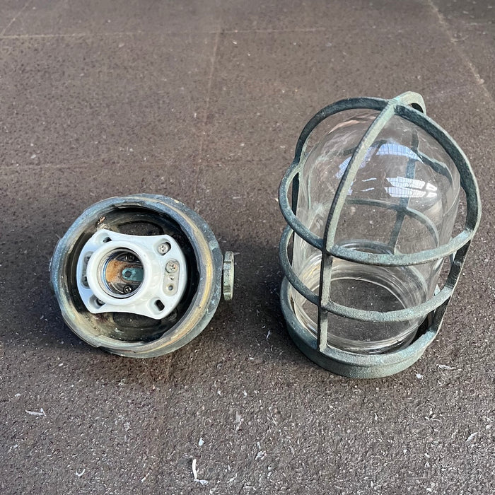 Salvaged marine cage light taken apart, cast brass body with ceramic lampholder beside the guard and glass dome