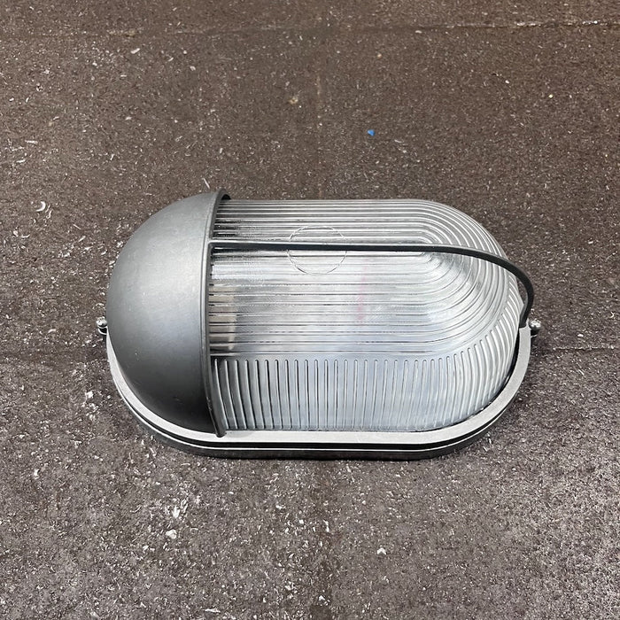 Black oval bulkhead light with eyelid shield and ribbed glass diffuser, front view