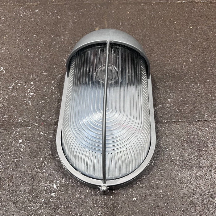 Side view of oval bulkhead light showing half-hood shield and guard bar